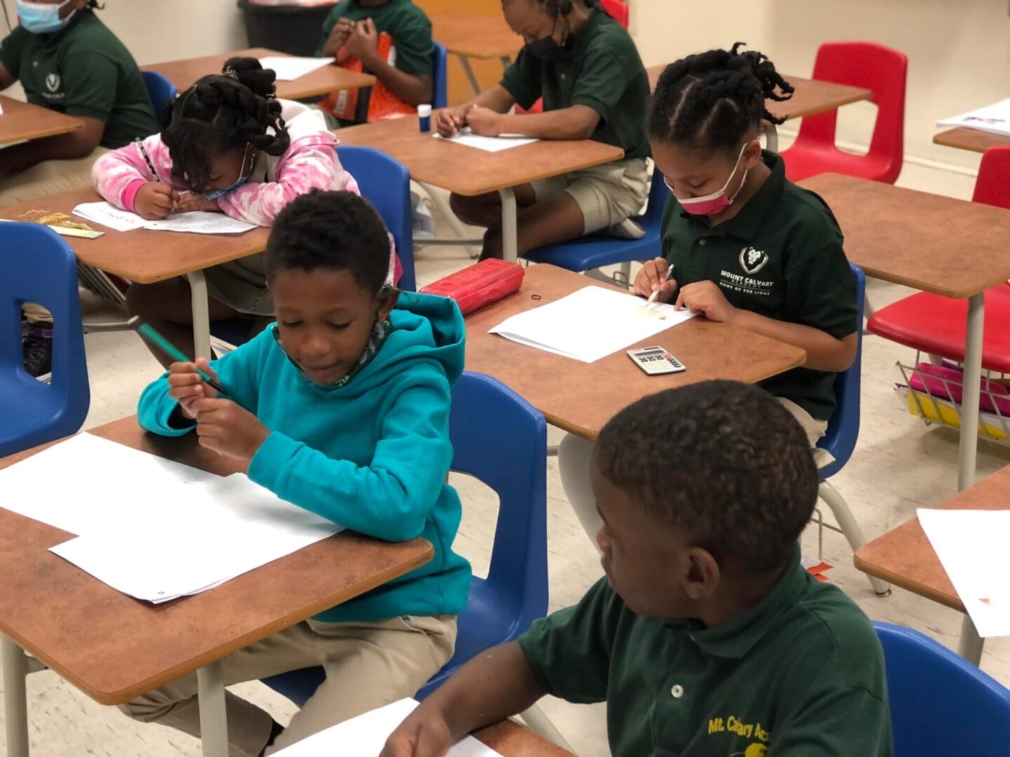 A group of children sitting at desks in front of papers.