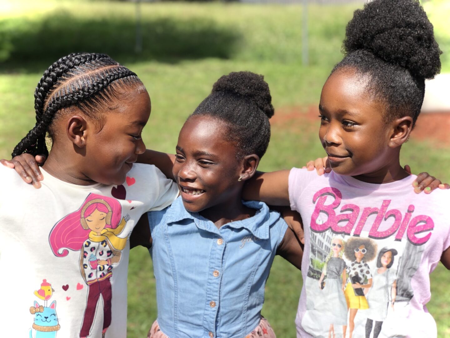 Three young girls are smiling and hugging each other.